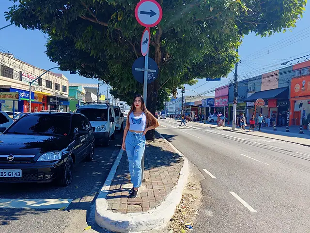 Mulher de calça jeans posando numa calçada arborizada do Itaim Paulista