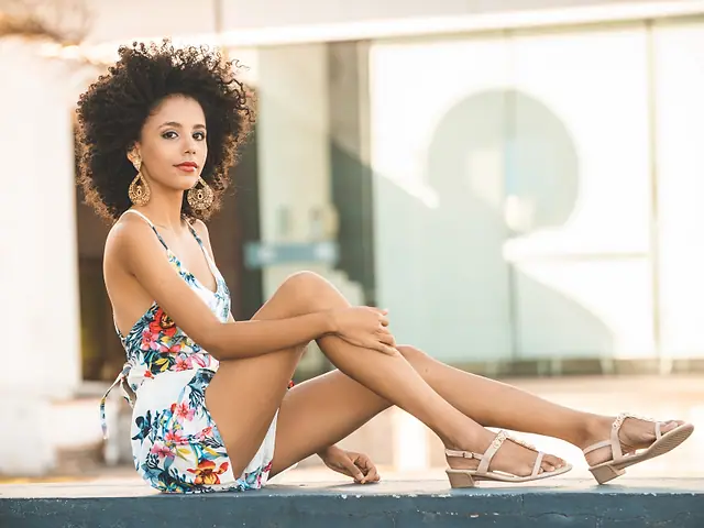 Mulher de vestido florido e sandálias sentada numa mureta